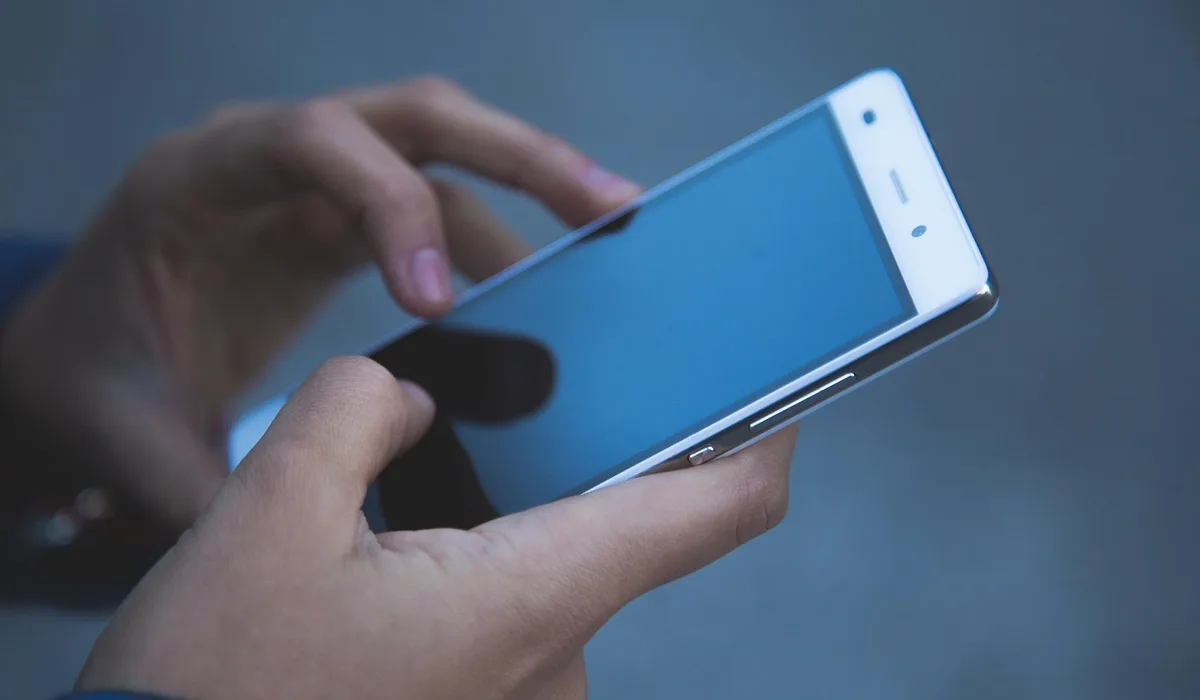 Hands holding and using a smartphone with a dark screen.