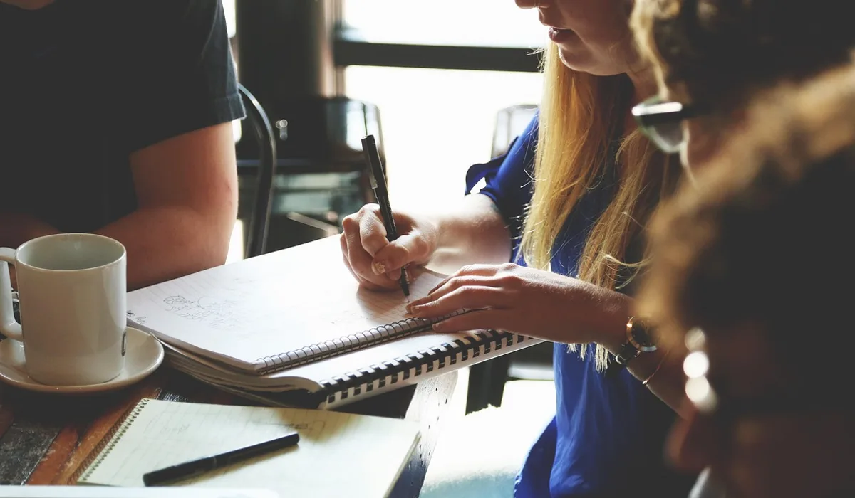 People gathered around a table with open notebooks, with one person writing by hand.